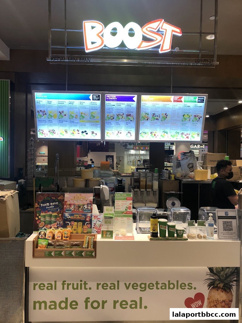 A Boost juice bar counter with digital menus displaying popular and protein drinks, and a slogan about real ingredients.