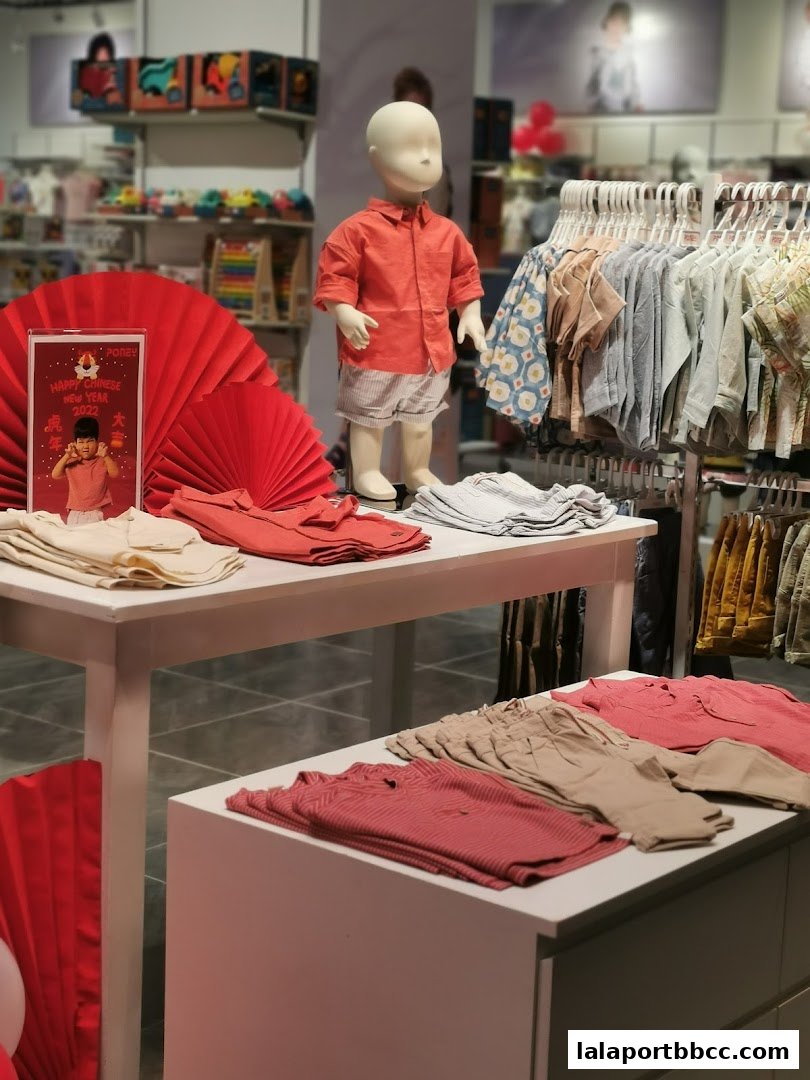 A child mannequin dressed in an orange shirt and shorts, with folded clothes and racks of children's apparel.