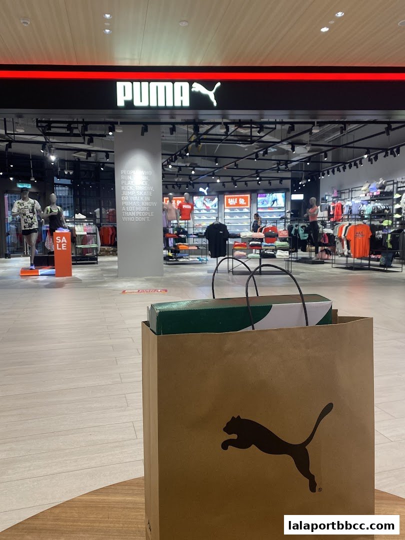 The entrance of a PUMA store with merchandise displayed and a shopping bag in the foreground.