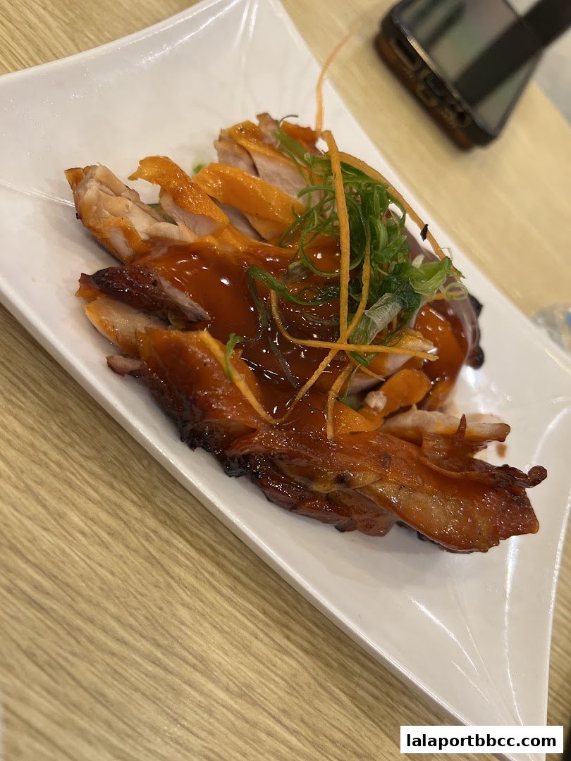 A plate of sliced roasted chicken with a glossy sauce and garnished with green onions and carrots.
