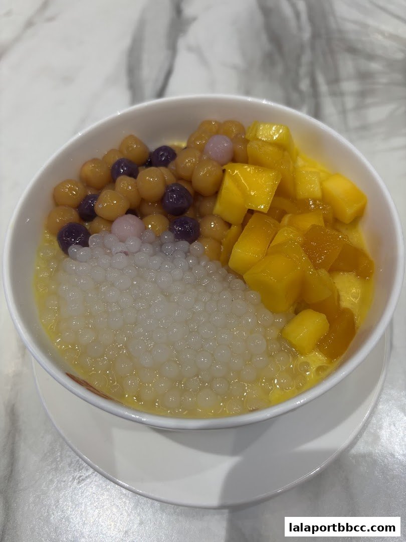 A bowl of dessert with mango, taro balls, and sago in a creamy yellow liquid.