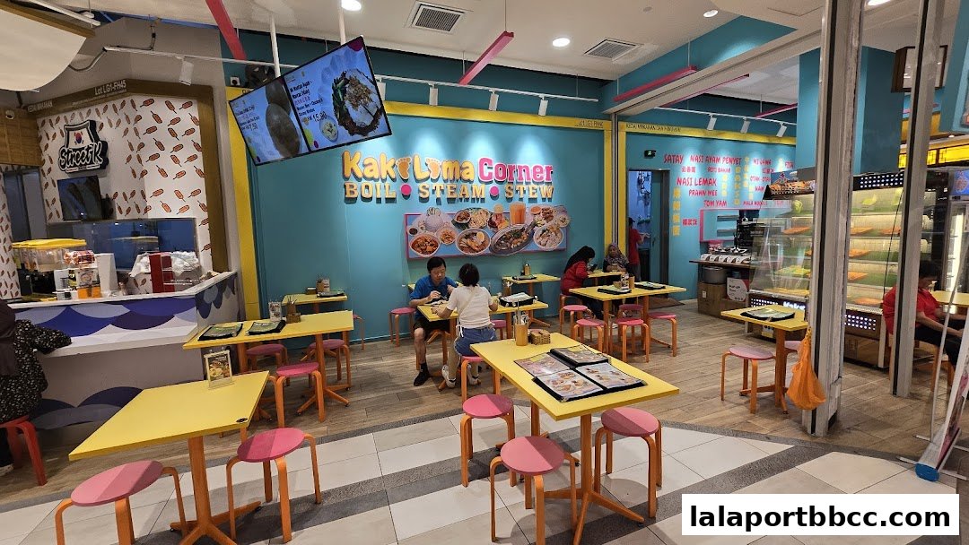 Interior view of Kaki Lima Corner restaurant with colorful tables and chairs, showing diners and food displays.
