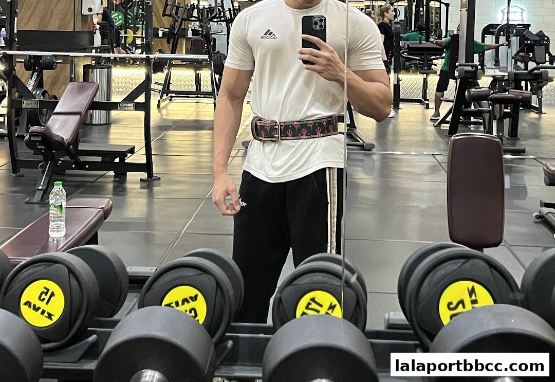 A person in workout gear takes a mirror selfie in a well-equipped gym.