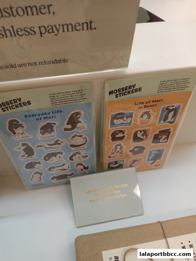 Packs of Mossery stickers featuring cats, with a sign offering a free sticker for a Google review.