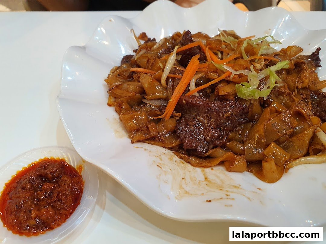 A plate of delicious stir-fried noodles with beef and a side of chili paste.
