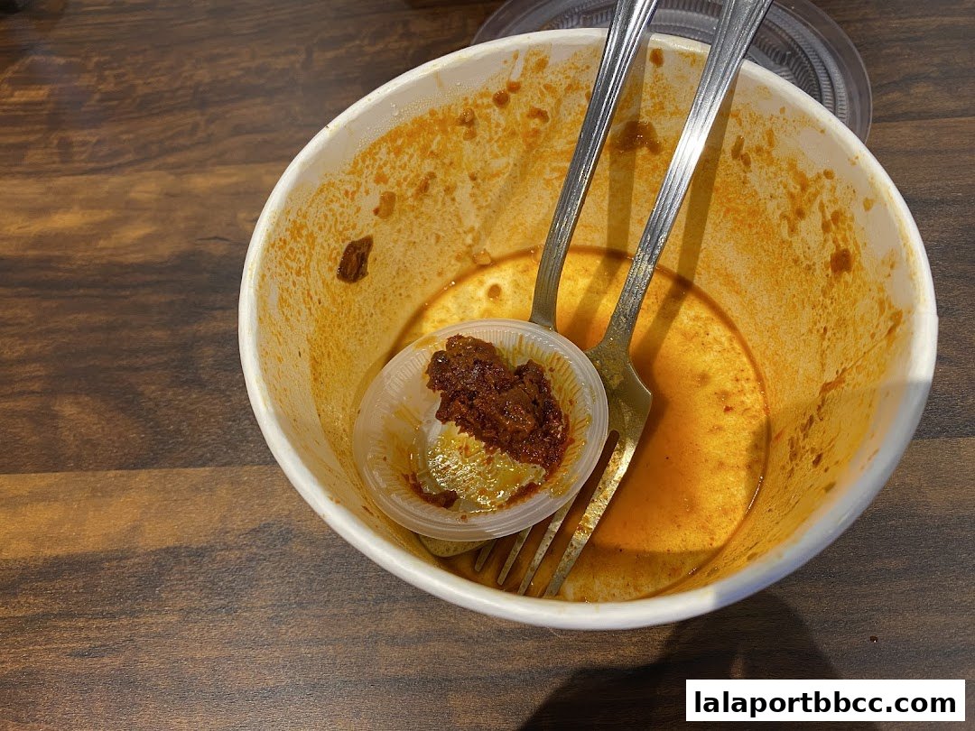 A nearly empty bowl with leftover curry sauce and a small container of sambal, with two forks inside.