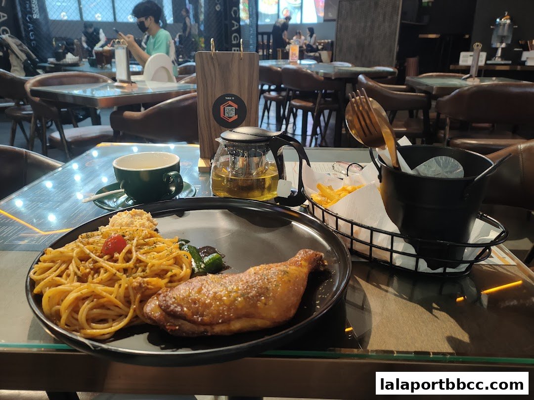A table setting at The CAGE - Duel Dine featuring a meal with pasta, chicken, fries, and tea.