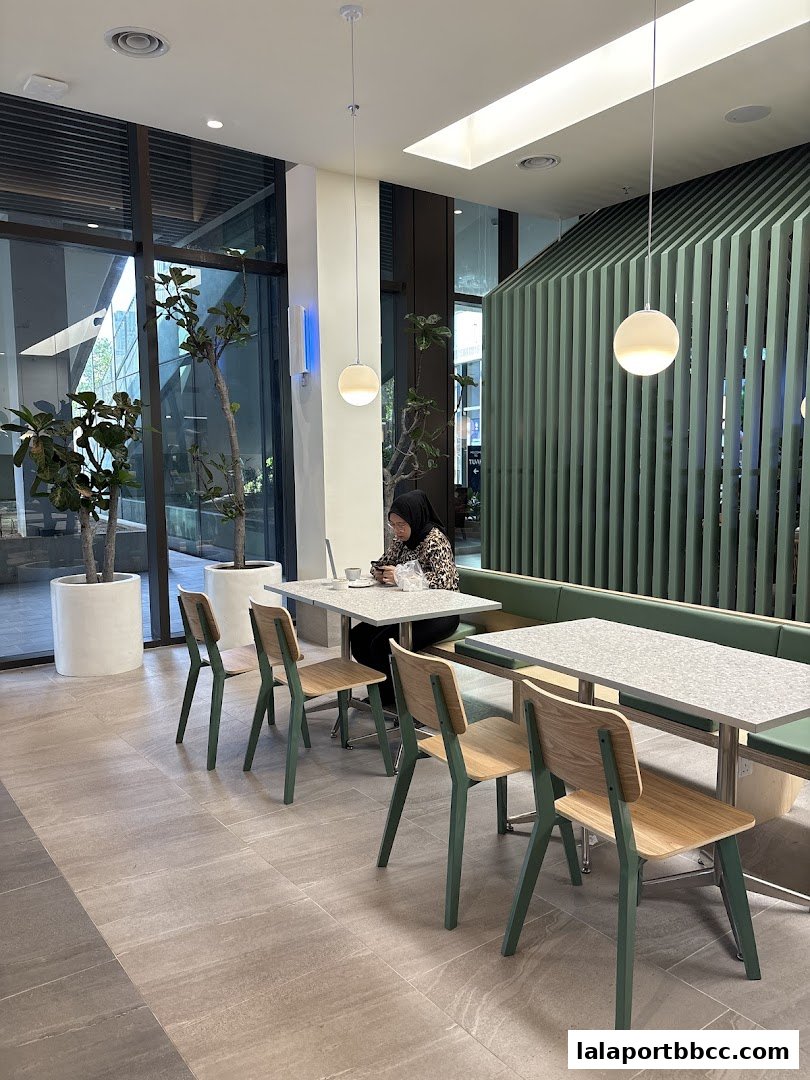 A modern cafe interior with green accents, tables, chairs, and plants.