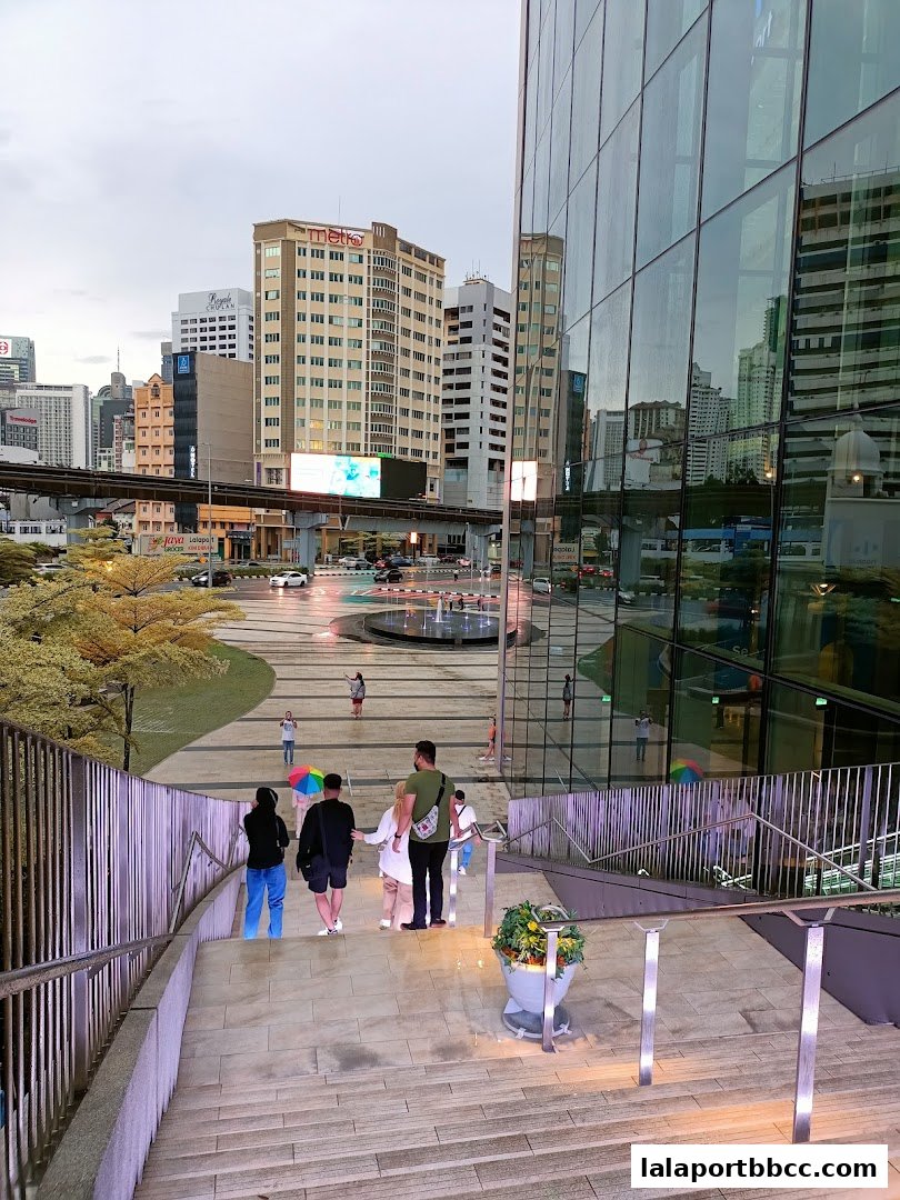 People walking down stairs towards a plaza with a modern glass building.