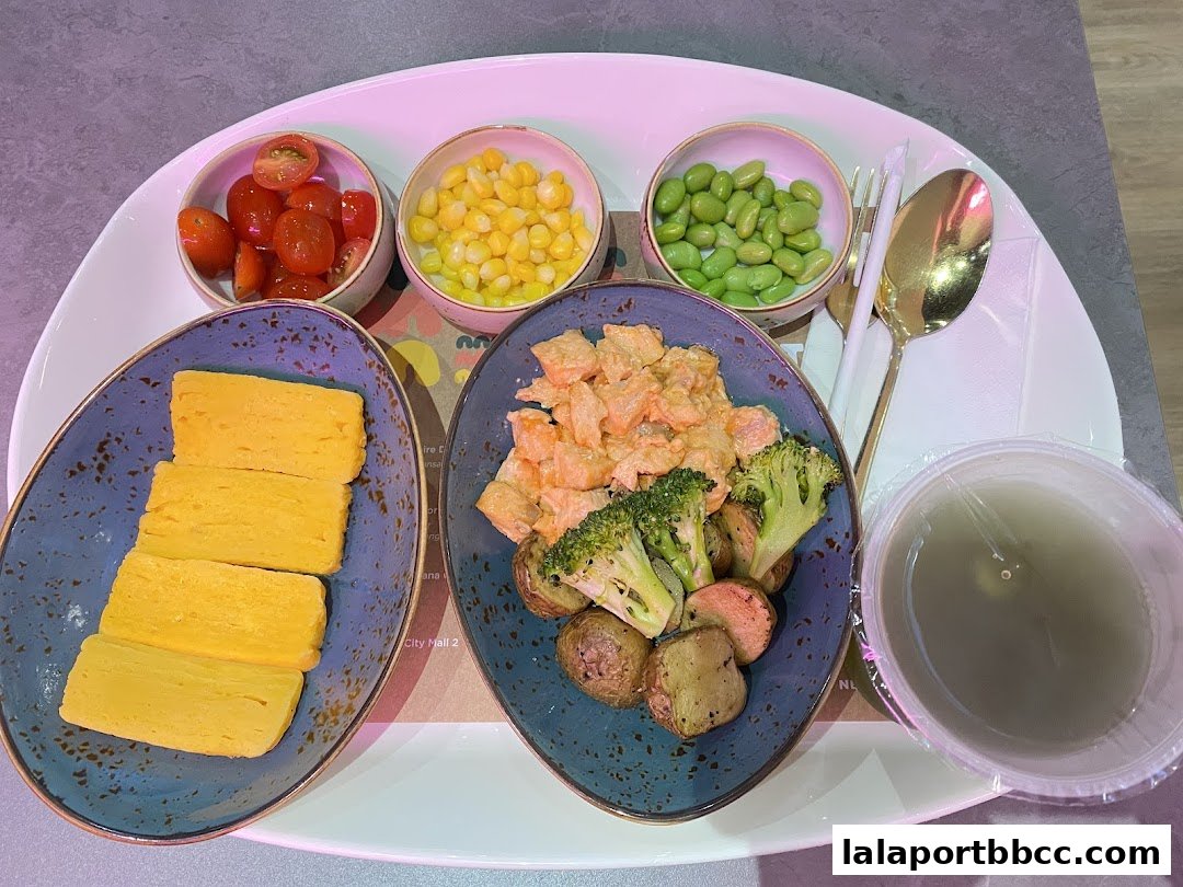 A meal set with tamagoyaki, salmon, vegetables, corn, edamame, and cherry tomatoes.