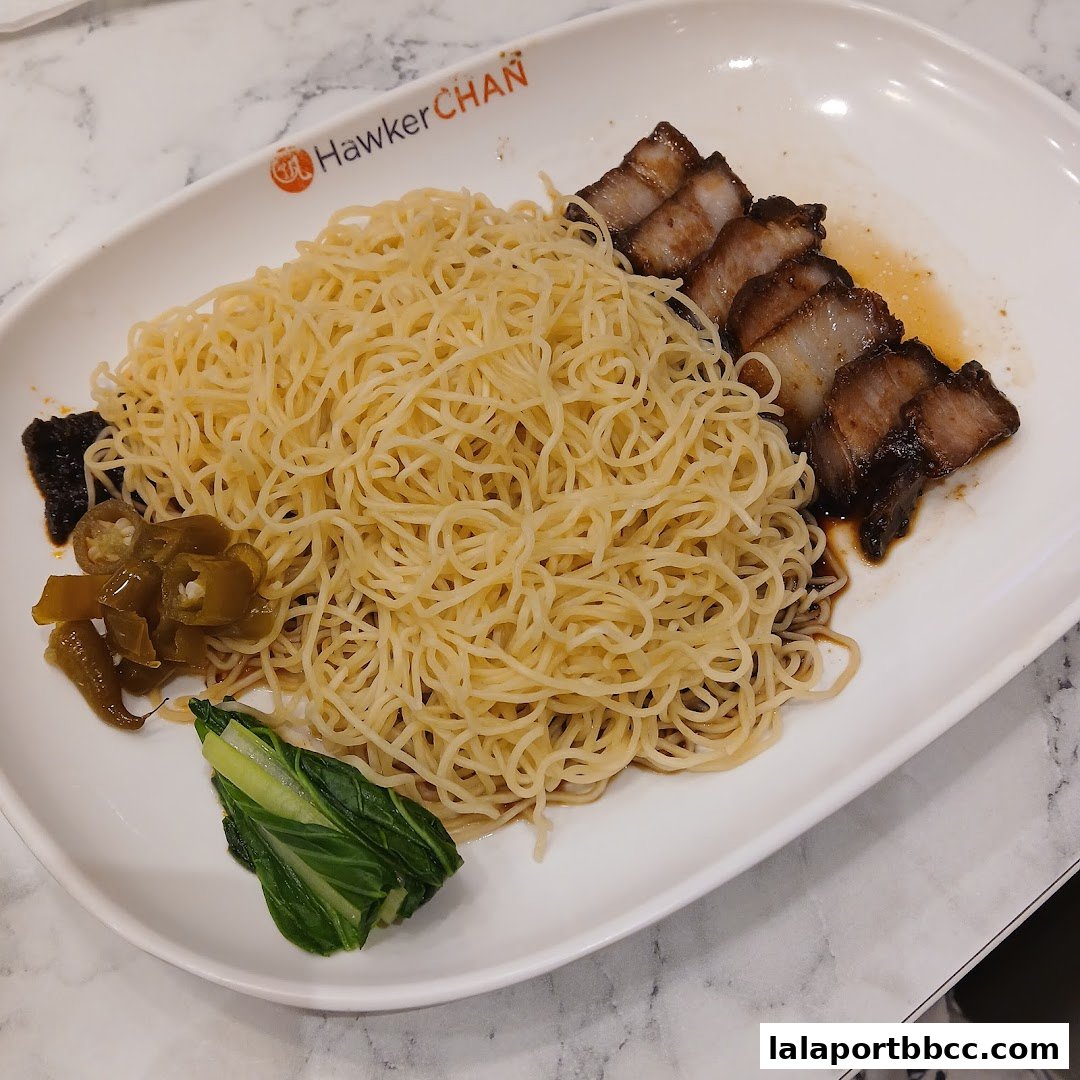 A plate of noodles with char siu pork, pickled chilies, and a side of greens.