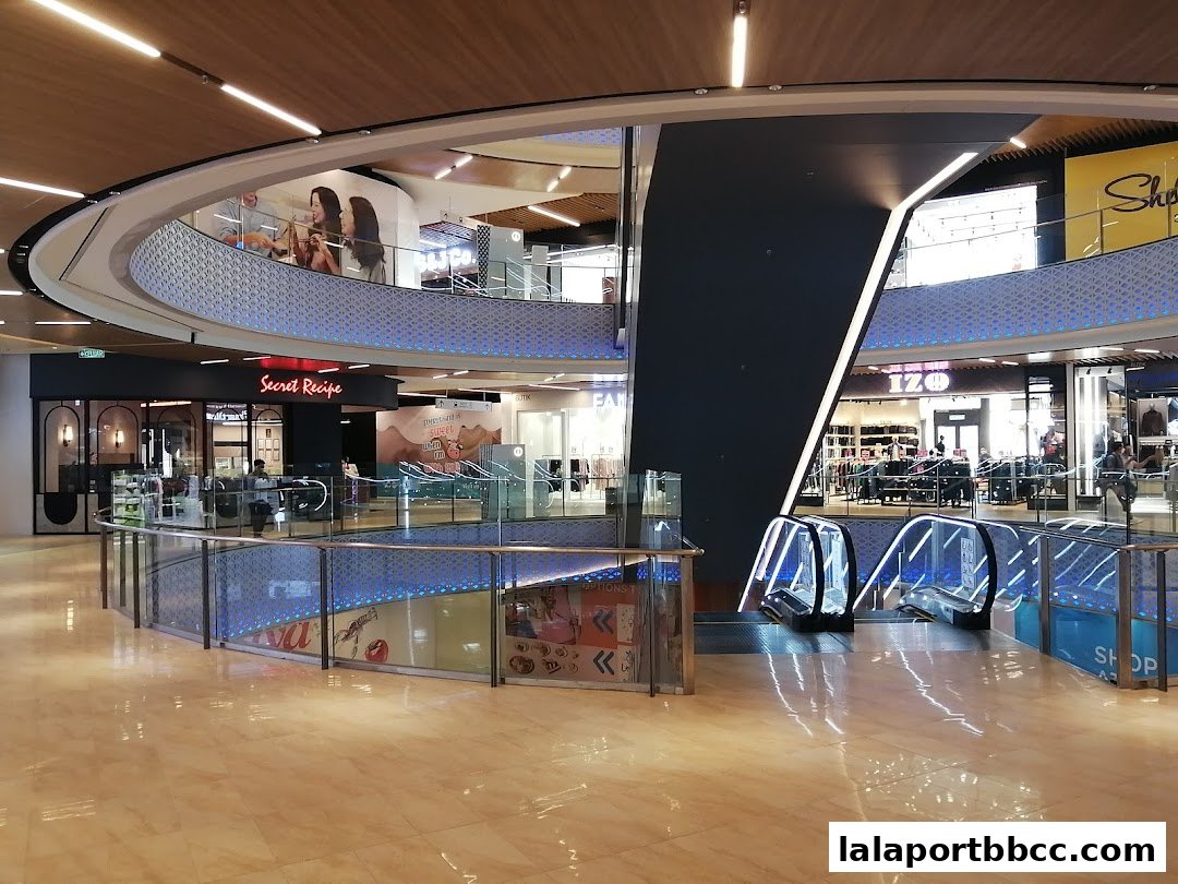 Interior view of a modern shopping mall with escalators and various shop fronts, including Secret Recipe.