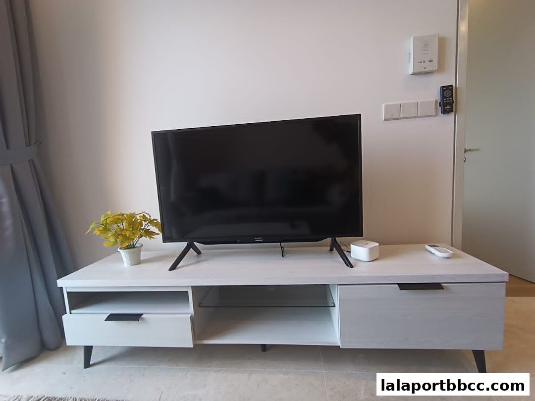 A modern TV stand with a television, plant, and remote controls in a room.