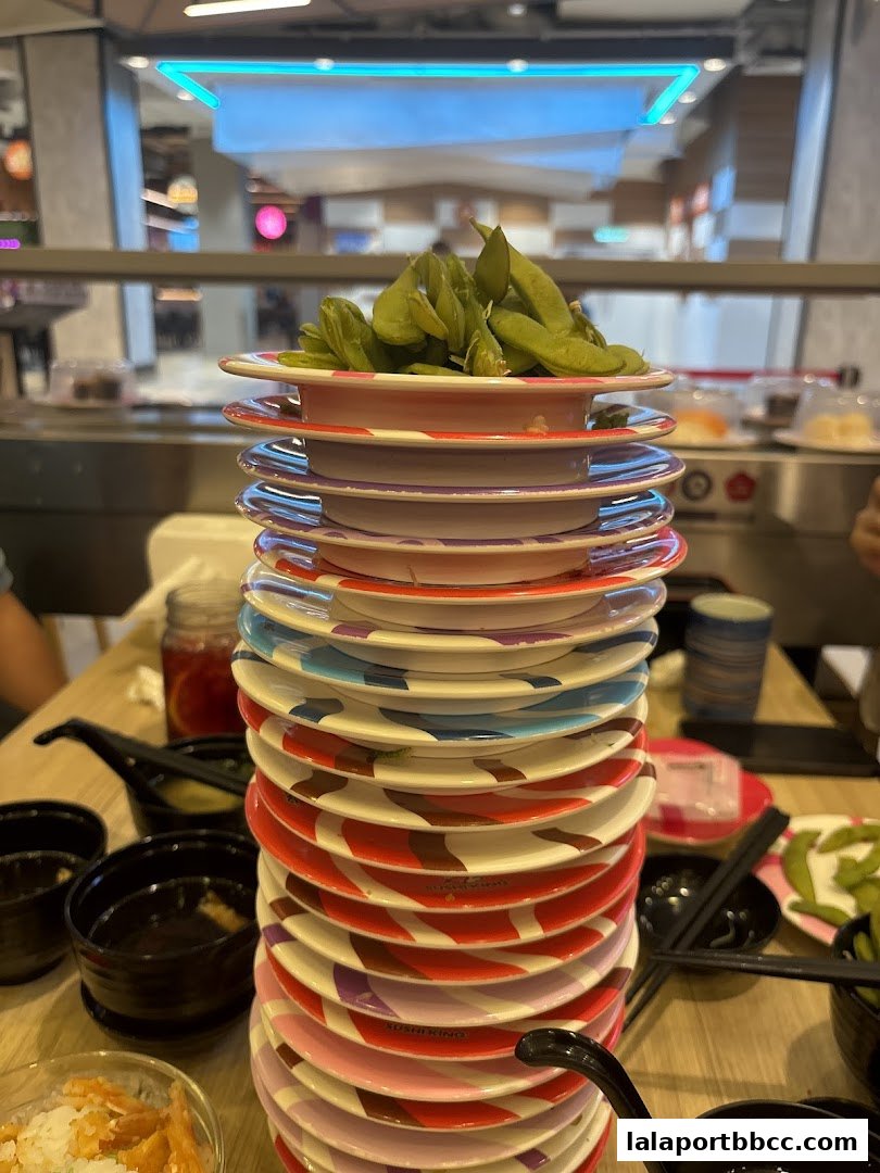 A tall stack of colorful sushi plates topped with edamame beans.