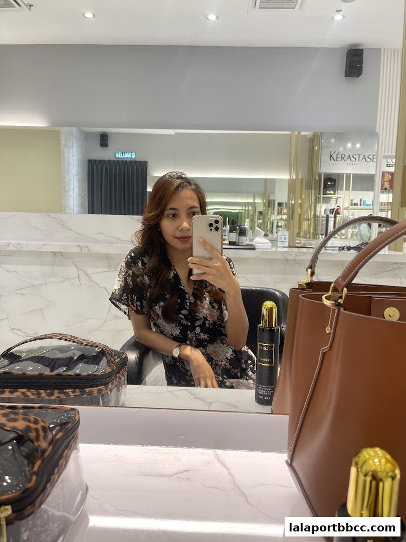 A woman takes a selfie in a salon, with Kérastase products visible in the background.