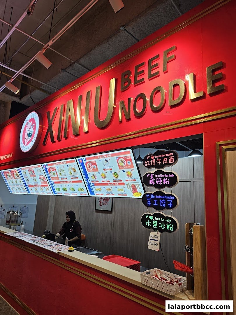 A food stall with a bright red sign displaying 'BEEF NOODLE' and illuminated menu boards.