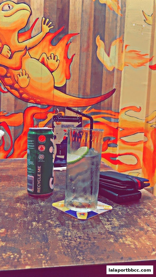 A refreshing drink with a can and a wallet on a table with vibrant wall art.