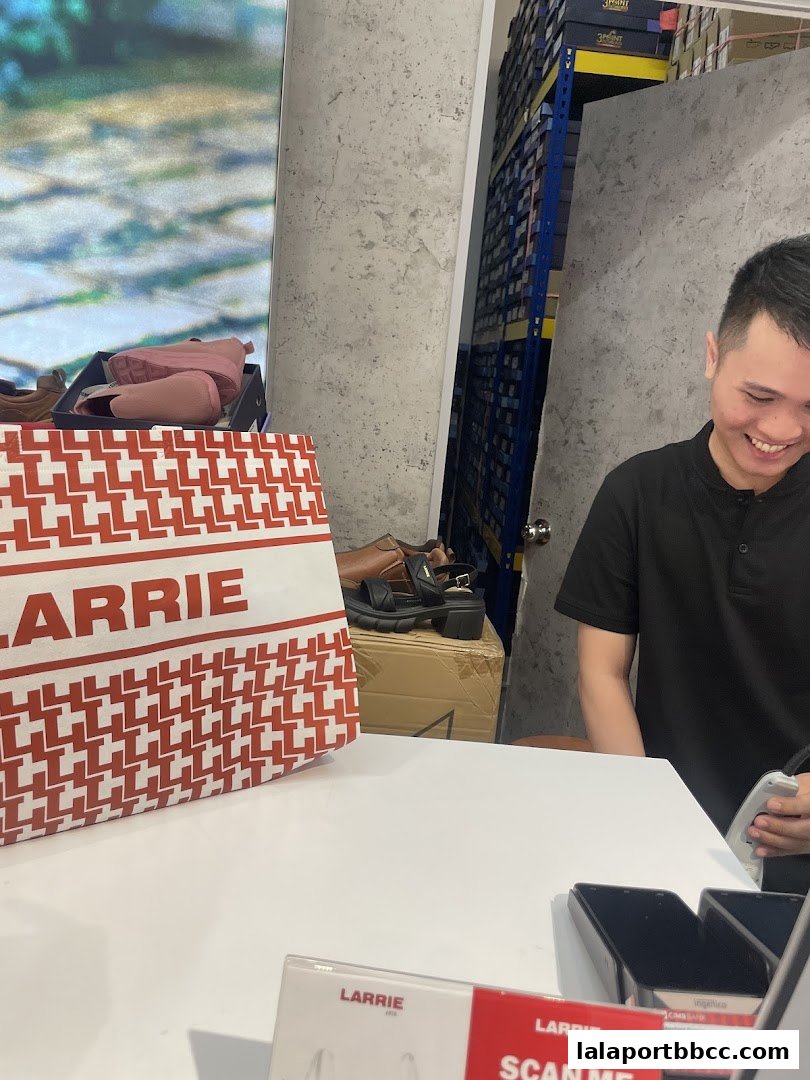 A smiling employee stands behind a counter with shoes and a shopping bag in a retail store.