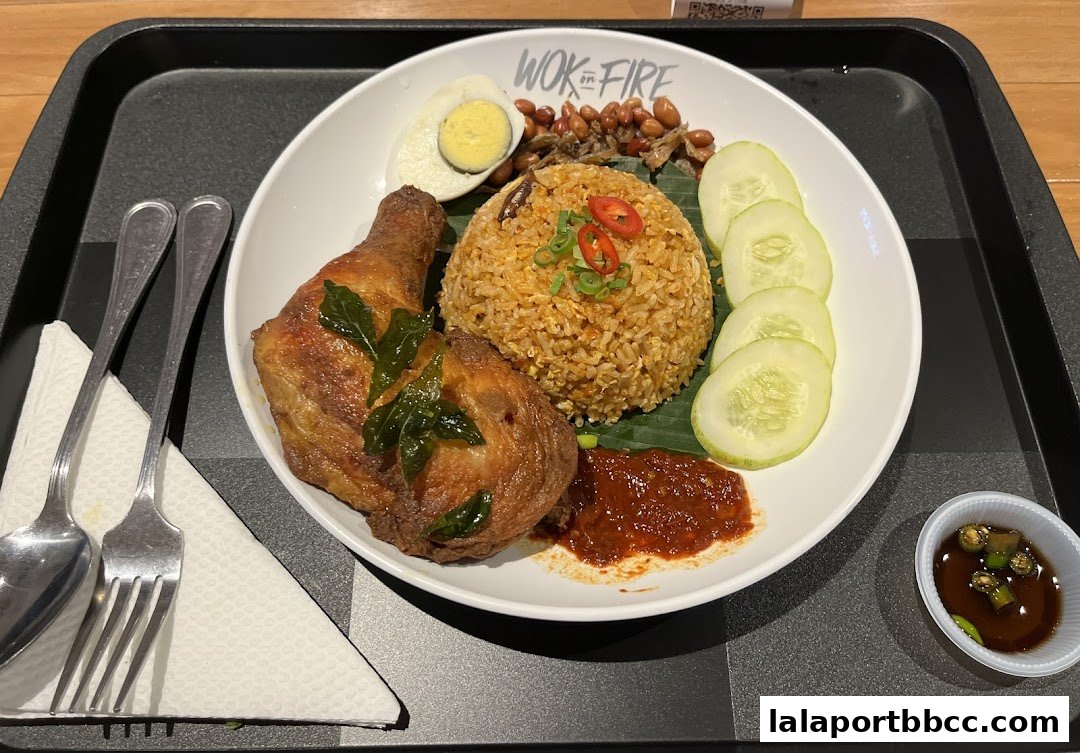 A plate of Nasi Lemak with fried chicken, fried rice, egg, peanuts, anchovies, cucumber, and sambal.
