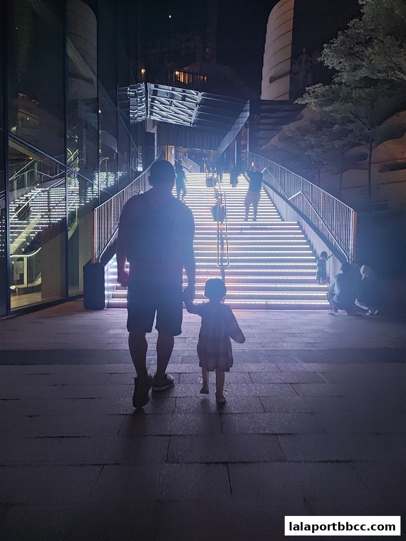 A father and child walk towards illuminated stairs at night.