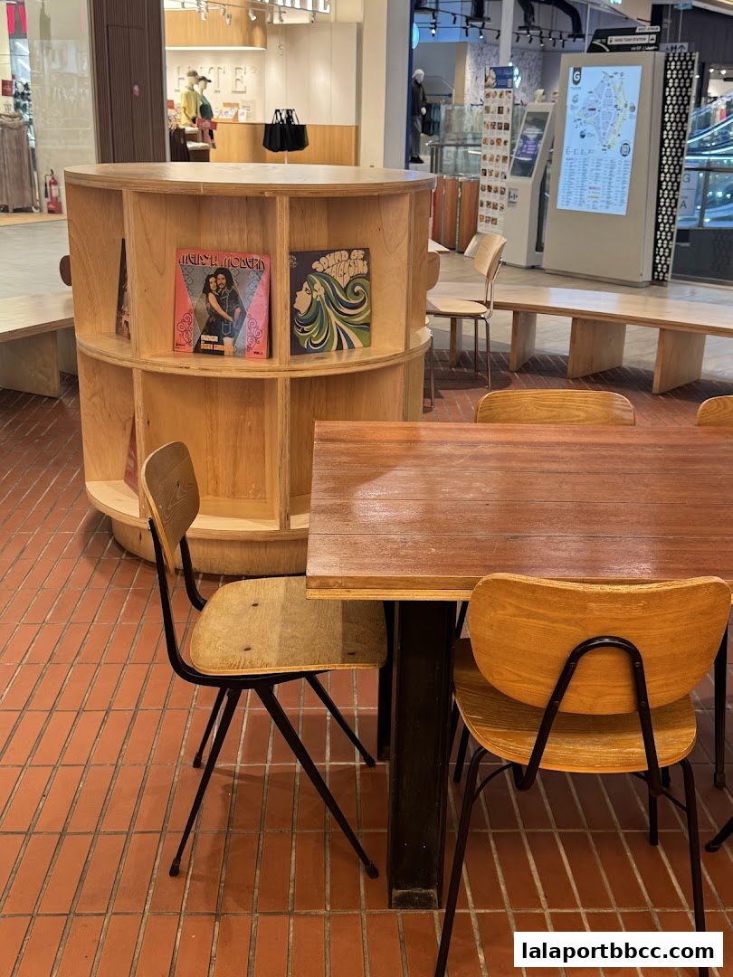 Interior shot of a cafe with wooden tables, chairs, and a circular bookshelf displaying records.