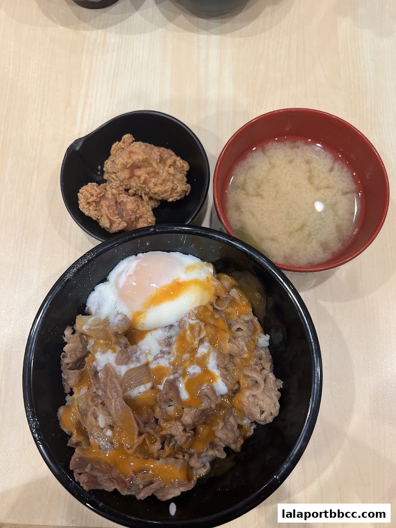 A close-up shot of a Japanese beef bowl with a side of fried chicken and miso soup.