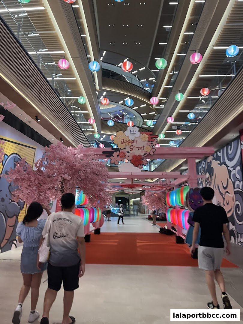 People walking through a festive indoor street decorated with cherry blossoms and lanterns.