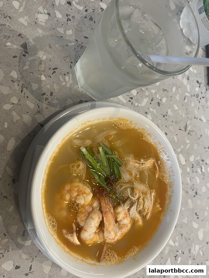 A bowl of delicious noodle soup with shrimp and a glass of iced drink.