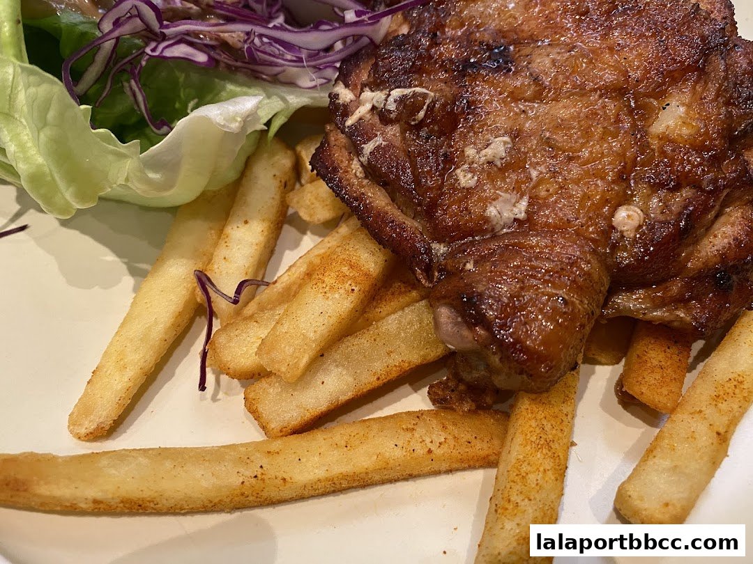A close-up of a delicious grilled chicken thigh with crispy fries and a side salad.