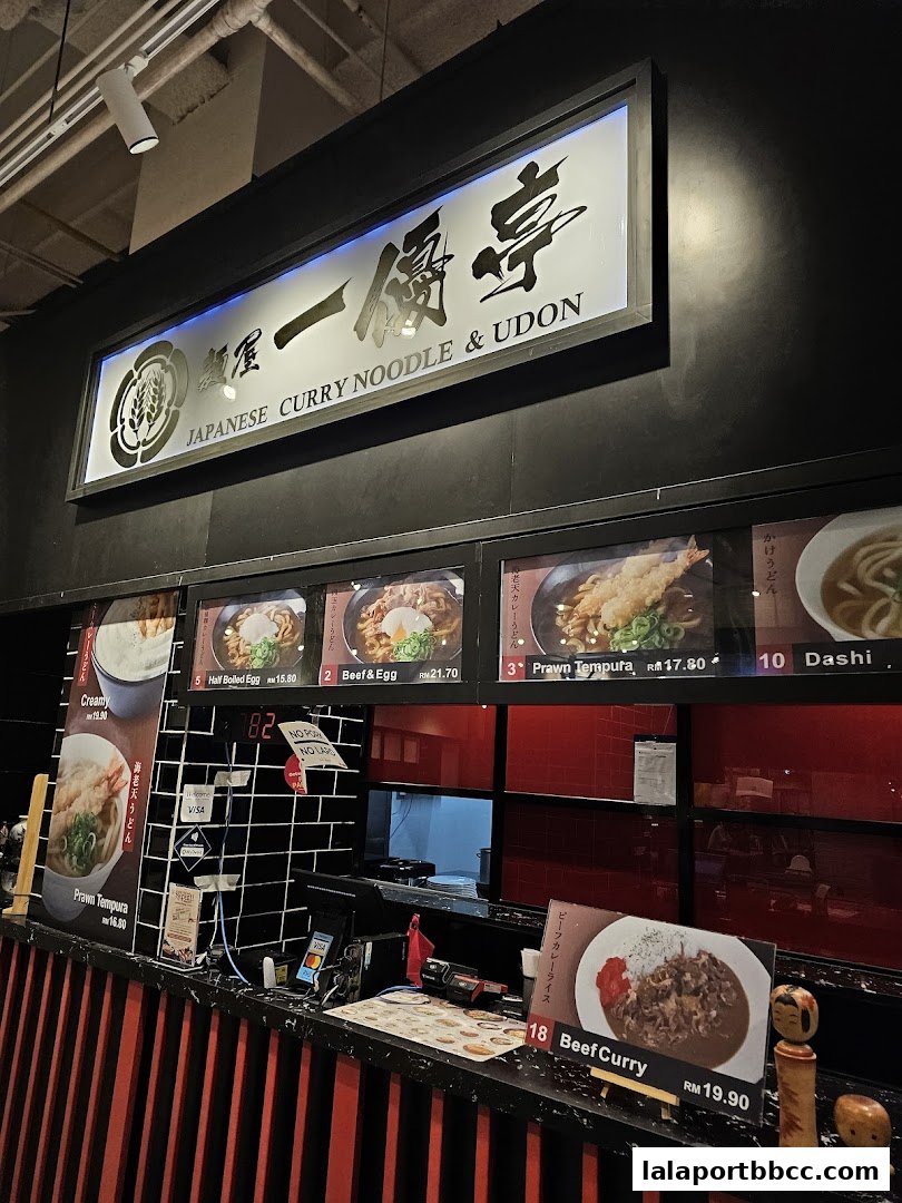 A food stall counter displaying Japanese curry noodles and udon dishes with prices.