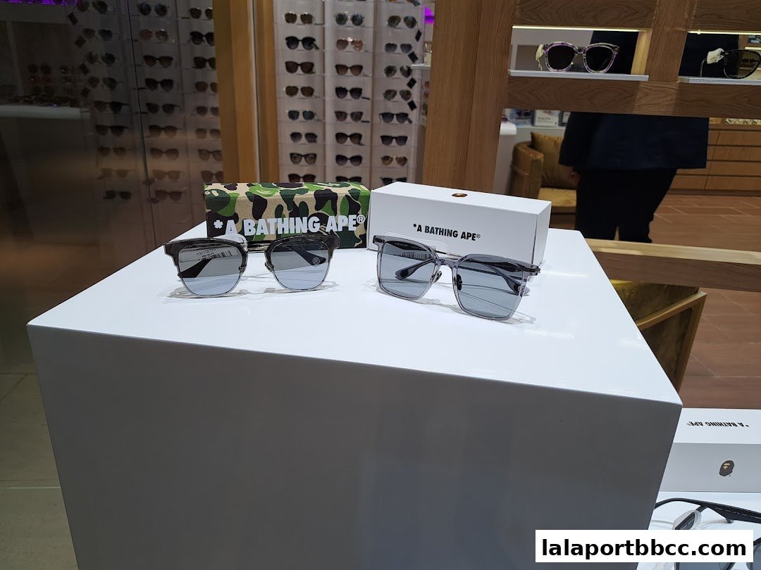 Stylish sunglasses displayed on a white pedestal with a camouflage A Bathing Ape case.