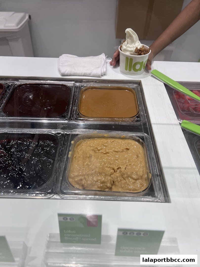 A cup of frozen yogurt with toppings and various dessert spreads behind it.