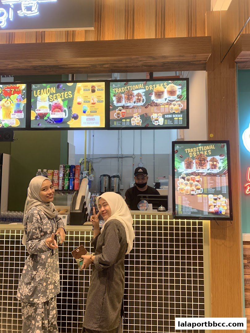 Two women posing in front of a beverage shop counter with menus displayed.