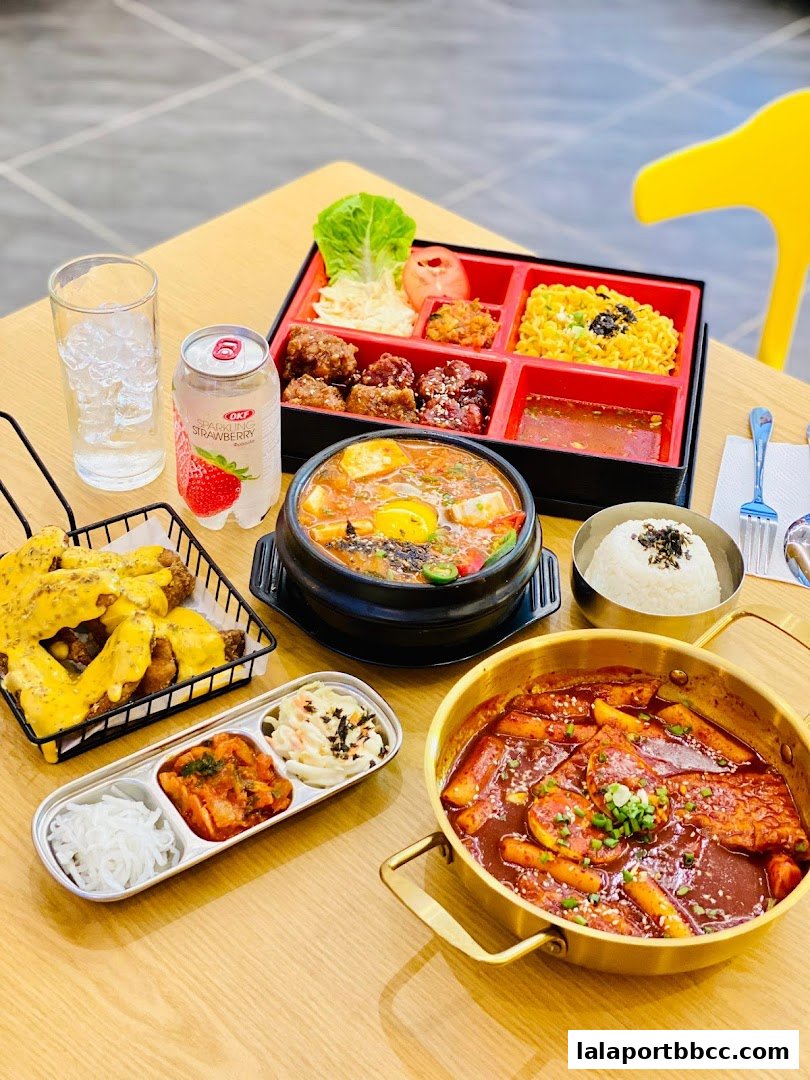 A table laden with Korean dishes including tteokbokki, fried chicken, and a bento box.