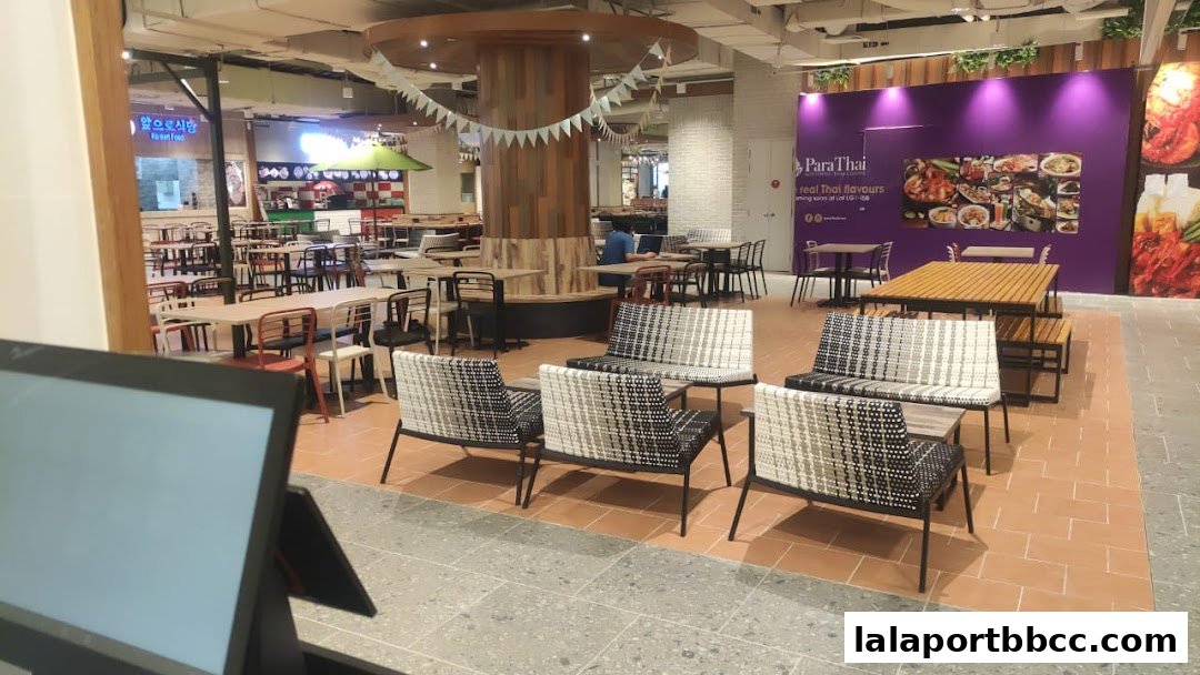 A modern food court with various seating areas and a Thai restaurant advertisement.
