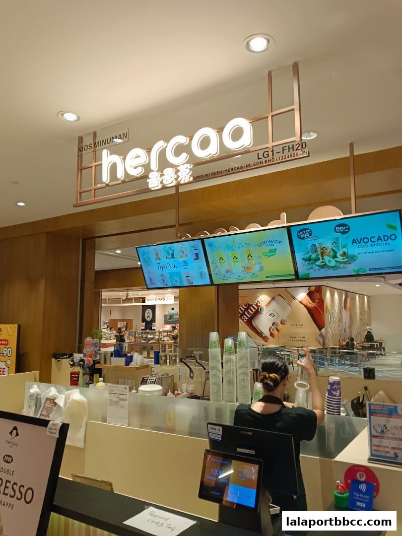 A modern beverage shop counter with a prominent 'hercaa' sign and digital menu displays.