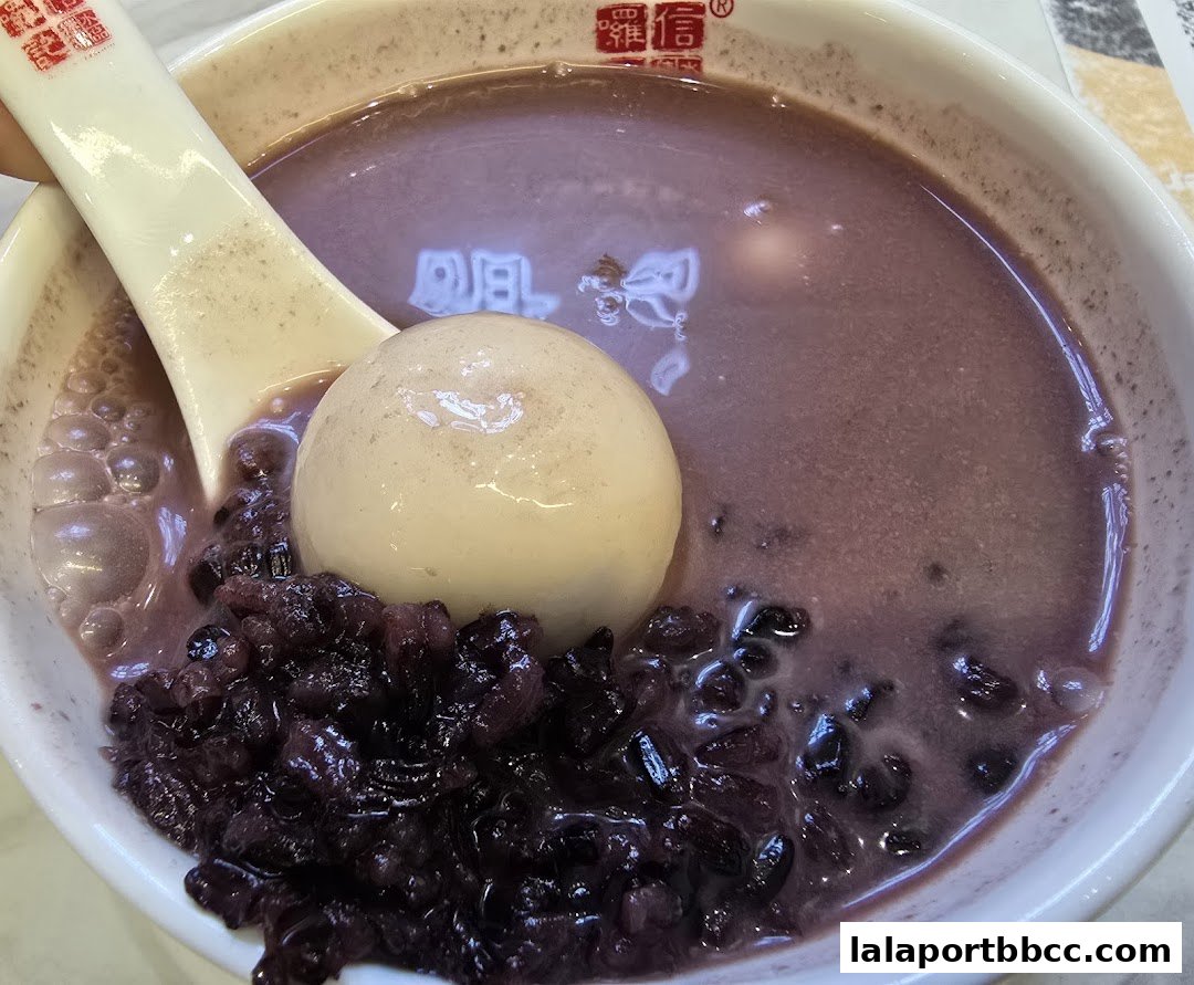 A close-up of a bowl of purple dessert with black rice and a white mochi ball.