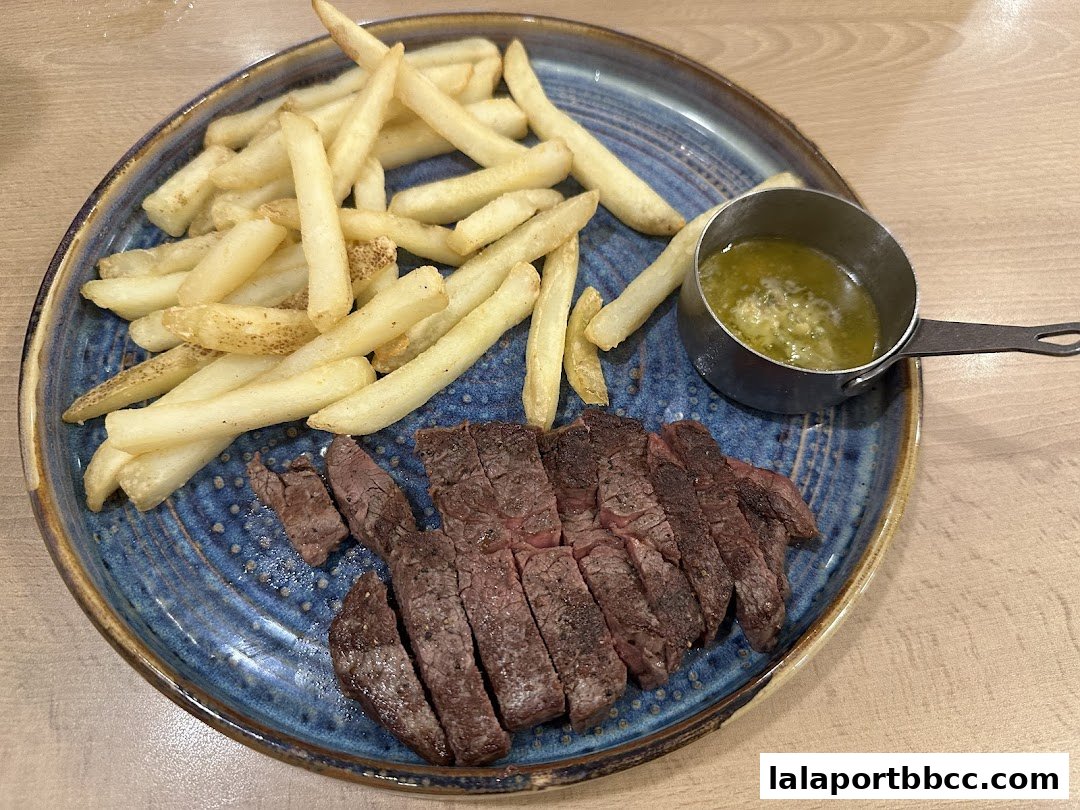 A plate of sliced steak and french fries with a side of sauce.