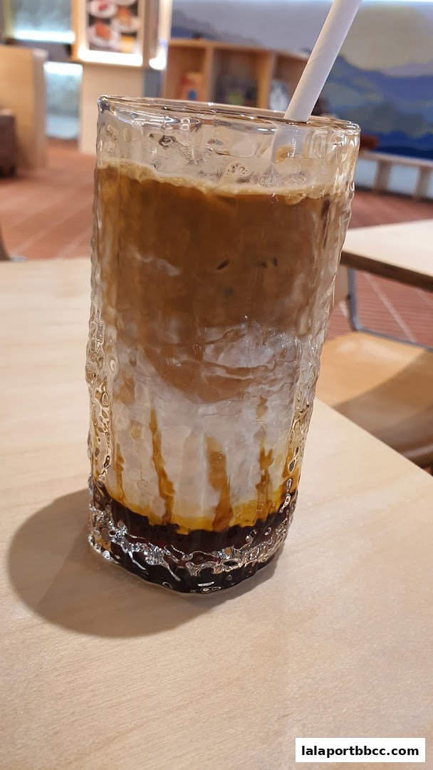 A tall glass of iced coffee with layers of milk, coffee, and syrup on a wooden table.