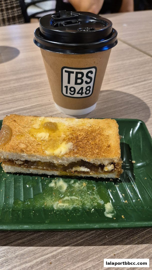 A close-up of a toasted sandwich with jam and butter, next to a coffee cup.