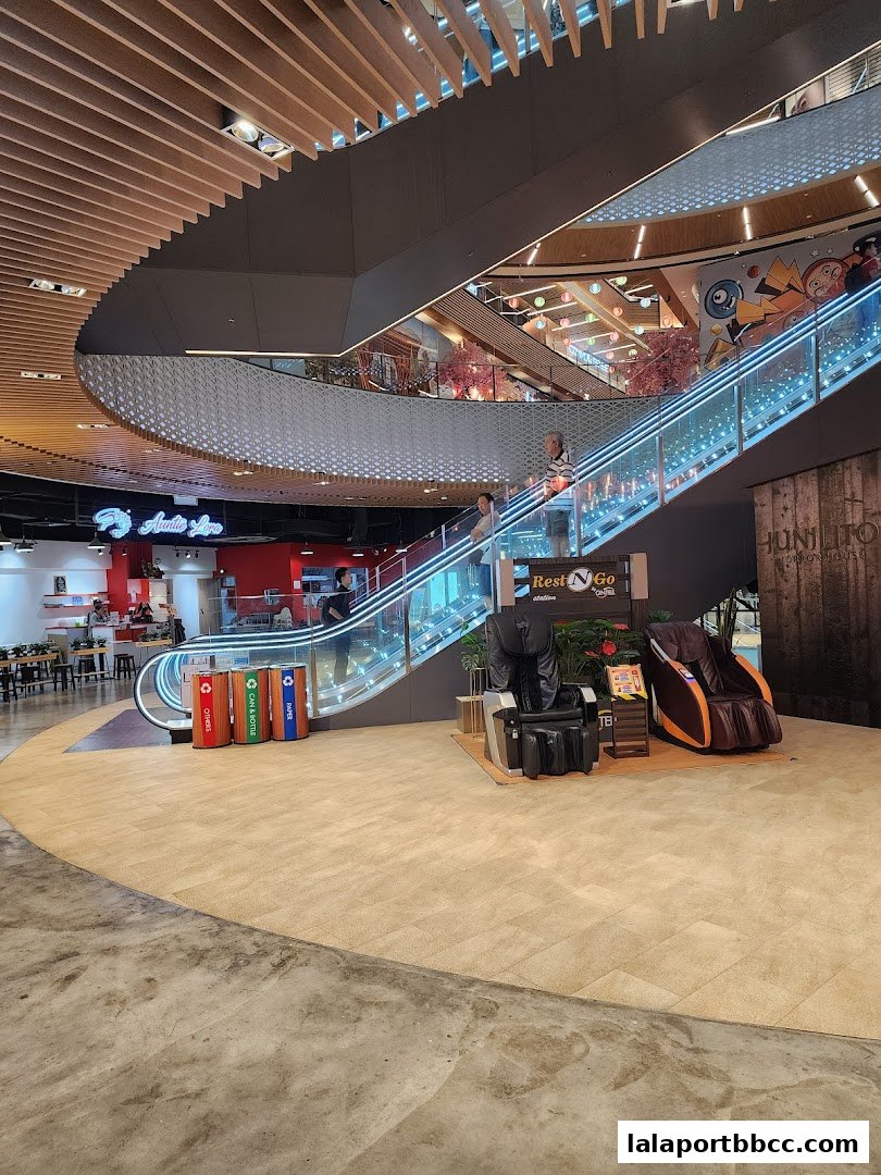 Interior view of a shopping mall with escalators, shops, and seating areas.