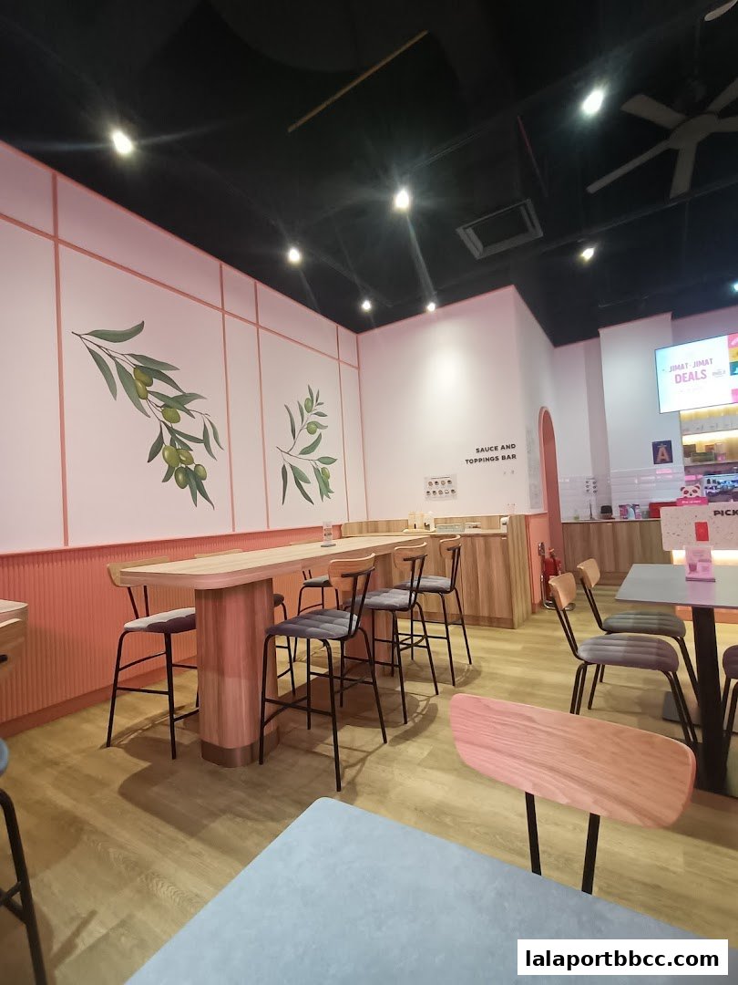Interior of a modern restaurant with high tables, chairs, and decorative olive branches on the wall.