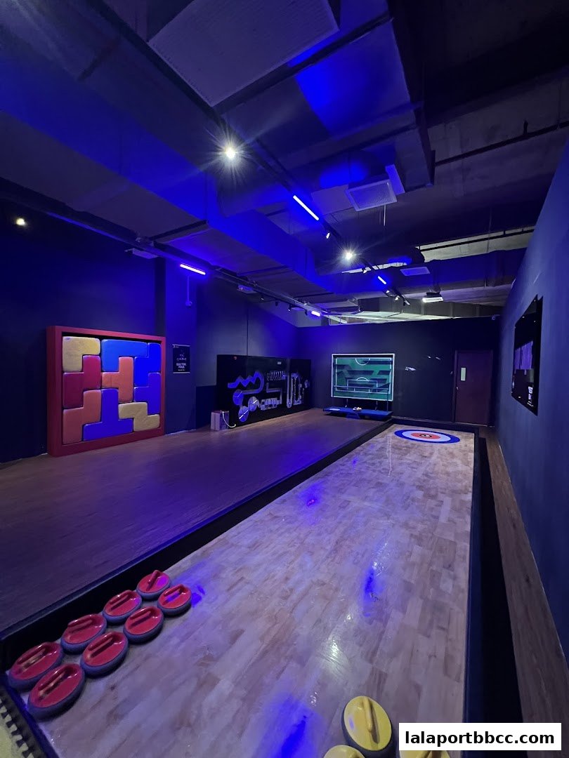 Interior of a game venue with shuffleboard and curling lanes, illuminated by blue lights.