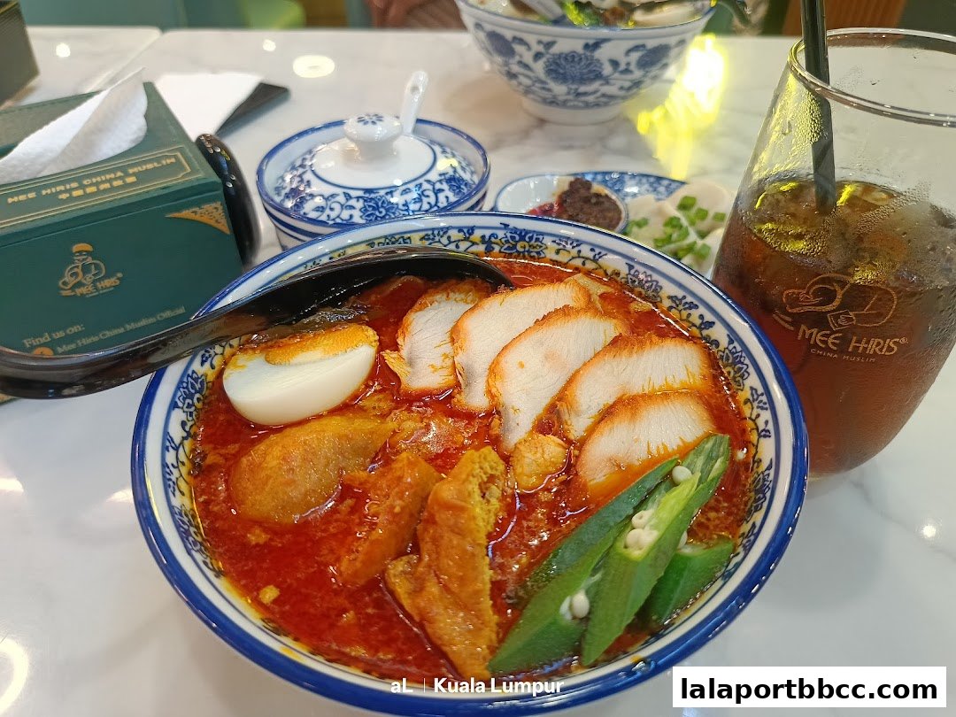 A bowl of delicious curry laksa with sliced chicken, egg, and okra, served with iced tea.