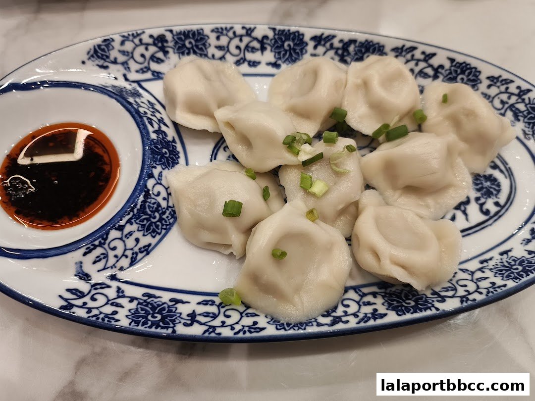 A plate of delicious dumplings with a side of dipping sauce, garnished with green onions.