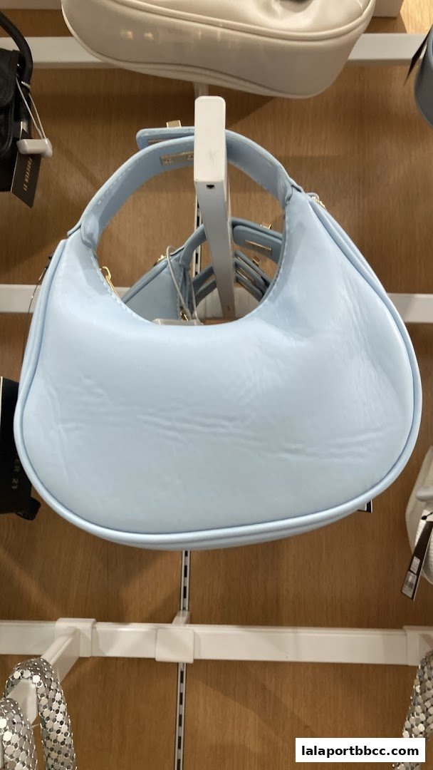 A light blue handbag with a curved handle is displayed on a shelf.