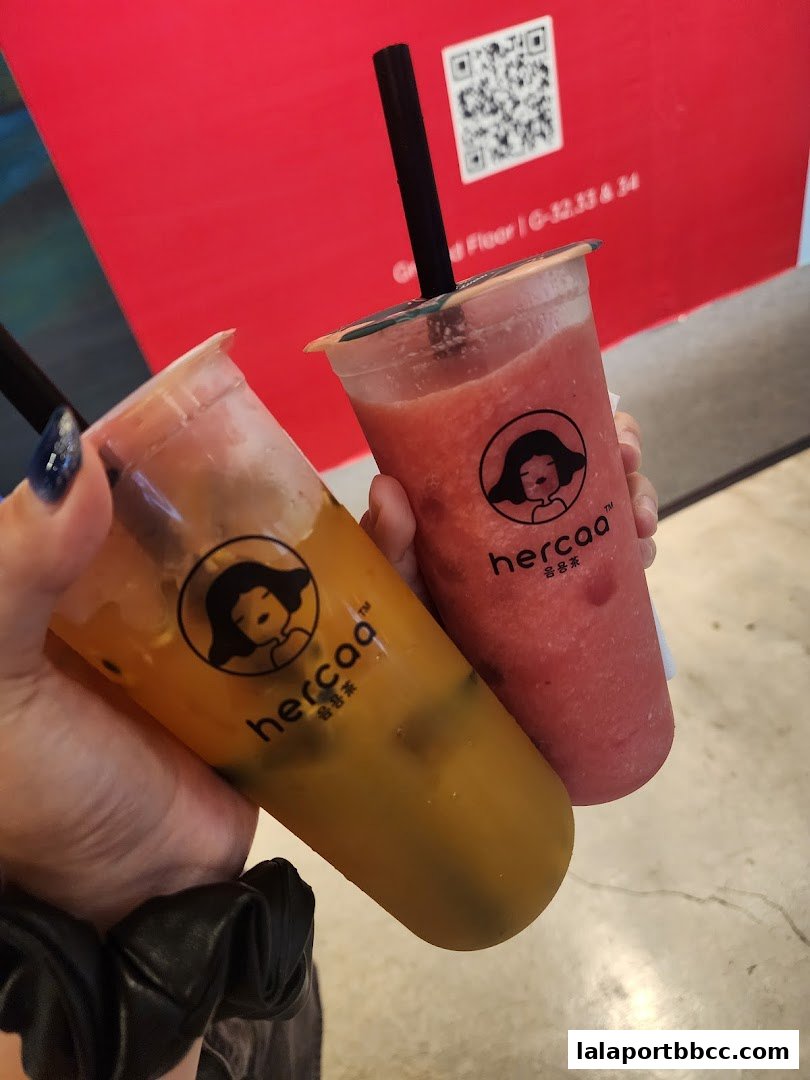 Two refreshing drinks from Hercaa Lalaport, one orange and one pink, held by hands.