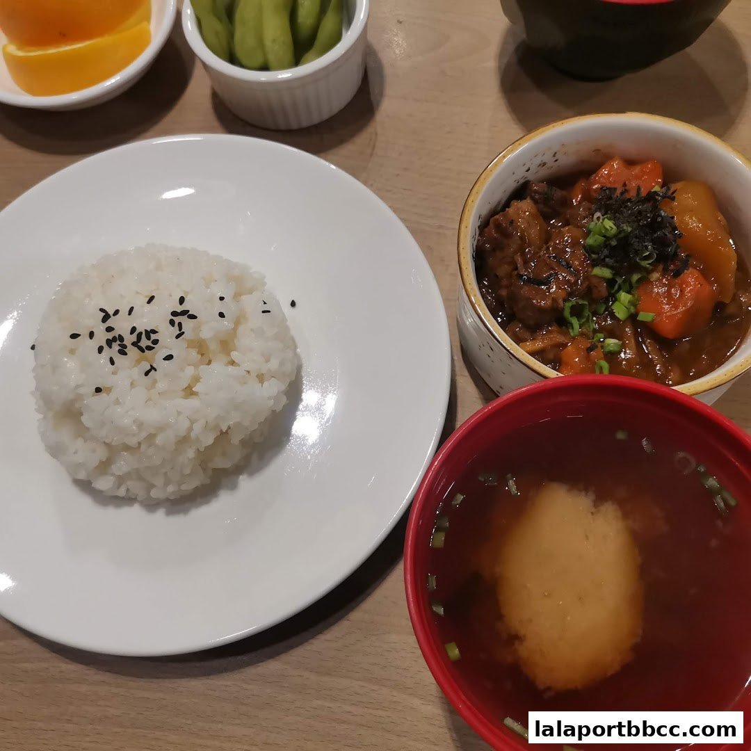 A close-up of a Japanese meal featuring rice, stew, soup, edamame, and orange slices.