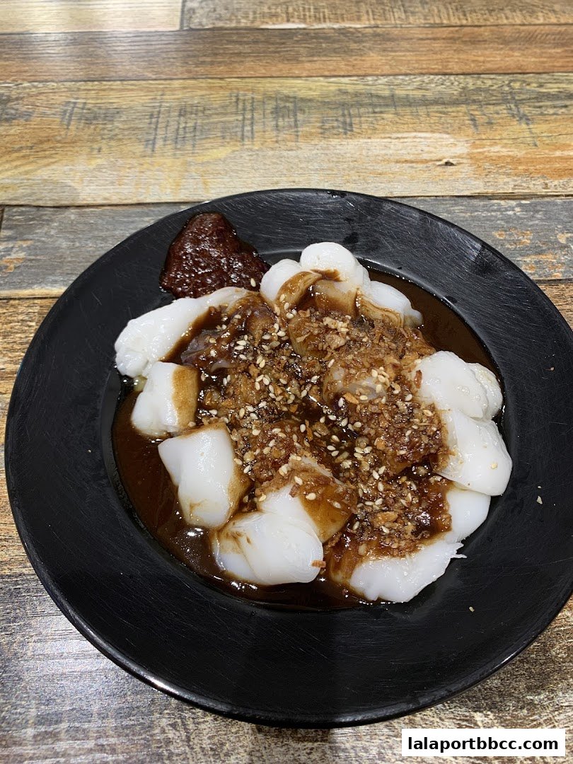 A close-up of chee cheong fun with soy sauce, chili paste, and fried shallots.