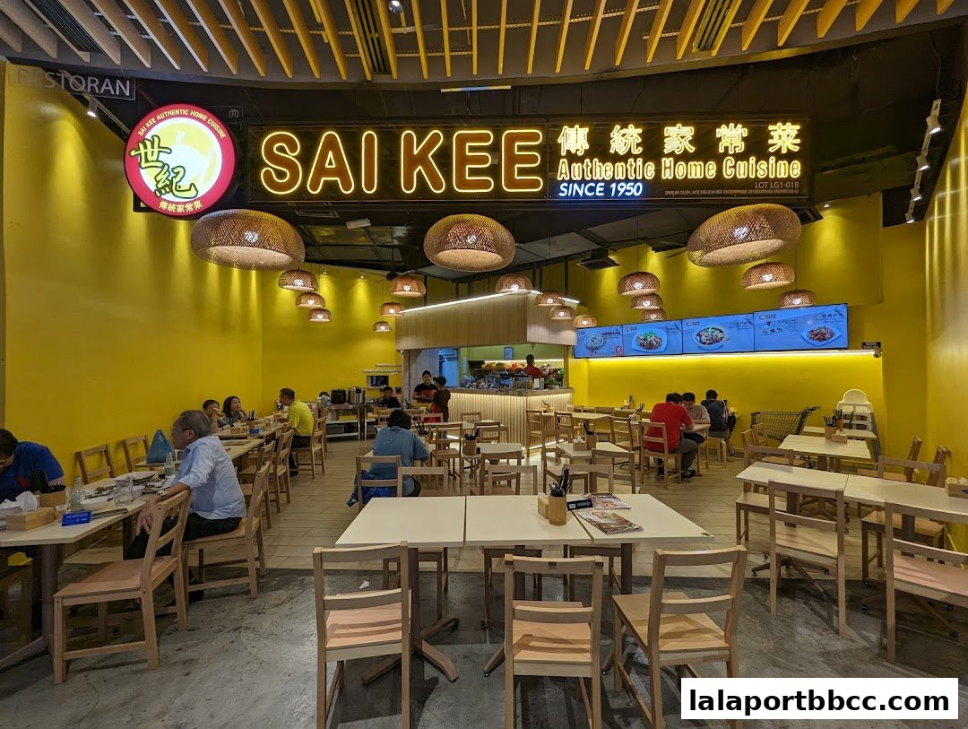 Interior of Sai Kee Restaurant with yellow walls, wooden chairs, and customers dining.